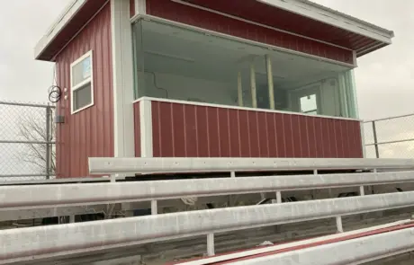 A small red-roofed press box with windows sitting atop metal bleachers.