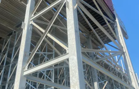 Looking up at a tall metal bleacher structure with a red-roofed box at the top against a blue sky.