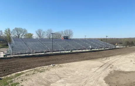 A daytime view of a large outdoor bleacher section beside a dirt track, with clear blue skies.
