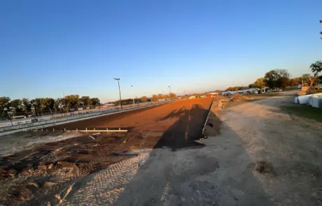 A construction site at dusk with clear skies, featuring a bare dirt ground and fencing in the background.